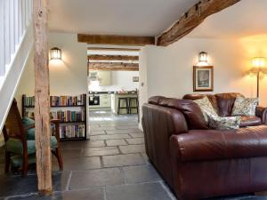 a living room with a leather couch and a book shelf at Swingletree Cottage in High Nibthwaite