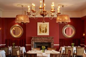 uma sala de jantar com paredes vermelhas e lustres em Ockenden Manor Hotel & Spa em Cuckfield