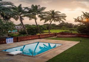 a swimming pool in a yard with palm trees at SaffronStays Amolee, Alibaug in Alibaug