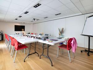 una sala de conferencias con mesas blancas y sillas rojas en ibis Styles Rennes St. Gregoire en Saint-Grégoire