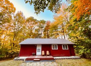 a red tiny house in the woods with two chairs at Escape to a 3-Bedroom Cabin in Lower Catskills in Woodridge