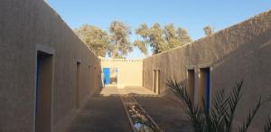 een steegje tussen twee gebouwen met bomen op de achtergrond bij Auberge Camping La Khaima in Merzouga