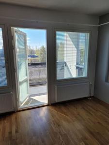 an empty room with two large windows and a room with wooden floors at Professori in Joensuu