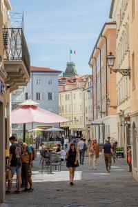 Un groupe de personnes marchant dans une rue avec des bâtiments dans l'établissement Hotel capitelli, à Trieste