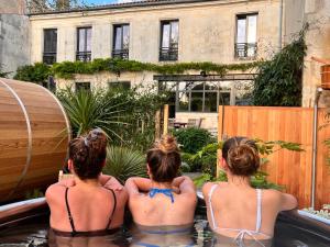 tres chicas sentadas en un jacuzzi en un patio trasero en Escale Rochelaise, gîte urbain avec SPA bain nordique et sauna tonneau en La Rochelle