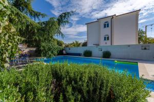 a swimming pool in front of a house with a building at Apartments Milivoj in Seget Vranjica