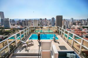 a woman standing on the balcony of a building with a swimming pool at São Paulo Tatuape, Affiliated by Meliá in Sao Paulo