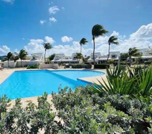 a swimming pool in a resort with palm trees at Villa Paradis Bleu Maison sur la plage, 2 chambres, piscines, tennis in Baie Nettle