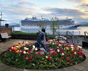 a statue of a woman in a flower garden with a cruise ship at clyde hub in Gourock