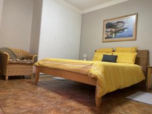 a bedroom with a bed with a yellow blanket and a chair at The Cottage in Somerset West