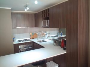 - une cuisine avec des comptoirs blancs et des armoires en bois dans l'établissement Departamento Resort Laguna del Mar, à La Serena 7 autres photos