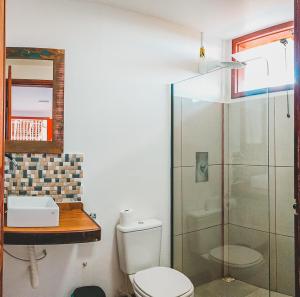 a bathroom with a toilet and a glass shower at Pousada Cordel de Itaúnas in Itaúnas