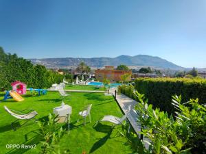 un jardin avec des chaises blanches et une aire de jeux dans l'établissement Villa Pollina, à Buseto Palizzolo