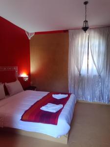 a bedroom with a bed with a red wall and a window at AUBERGE DES ANGES in Zrigat