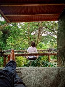 une personne assise sur une terrasse couverte avec ses pieds sur une balustrade dans l'établissement ECO Cabin - TANOA Minca, à Minca