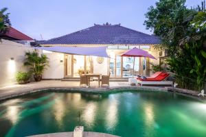 a swimming pool with a table and an umbrella at Ambermoon Villas in Seminyak