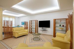 a living room with two yellow chairs and a flat screen tv at Hotel Sabbia d'Oro in San Vito lo Capo