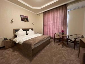 ein Hotelzimmer mit einem Bett, einem Tisch und einem Fenster in der Unterkunft Khan Palace Hotel in Yakkasaray