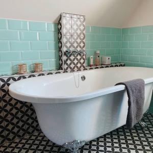 a large white bath tub in a bathroom with green tiles at Volledig gerenoveerde luxe gastsuite met ontbijt in Vlissingen