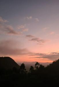 - une vue sur un coucher de soleil avec des nuages et des arbres dans l'établissement Chalé Milão Caravaggio, à Santa Teresa