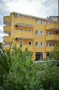 um edifício amarelo com árvores em frente em Apartmani Alexandra em Budva