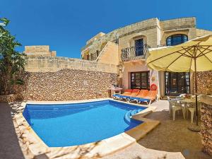 a swimming pool with an umbrella next to a house at Razzett ta' Leli Holiday Home in Xagħra