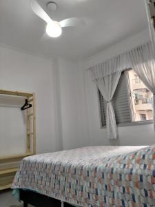a bedroom with a bed with a ceiling fan and a window at Apartamento Pé na Areia - Praia Grande - SP, Aviação in Praia Grande