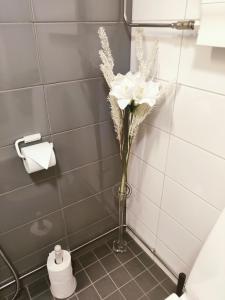 un jarrón con flores blancas en la esquina de un baño en Joutjärven Studio Apartment, en Lahti