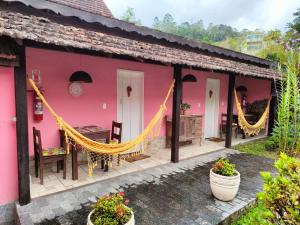 a pink house with a hammock and a table at Pousada Lírio do Campo in São Pedro da Serra