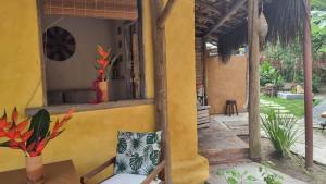 a yellow house with a chair and a window at Casa Namoa Pousada in Ilha de Boipeba