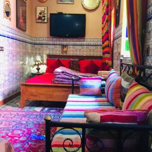 een slaapkamer met een bed met kleurrijke kussens en een televisie bij ALMARKAB Riad in Marrakesh