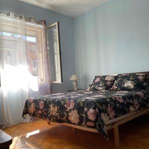 sypialnia z łóżkiem z kwiatową narzutą i oknem w obiekcie Rita's Home w Tiranie
