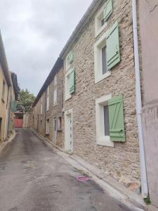 Roquetaillade的住宿－Gîte chaleureux au cœur du village，街道上一座带绿色百叶窗的石头建筑
