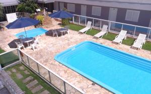 a swimming pool with chairs and a table and umbrellas at Hotel Pousada Ilha do Mar Bombinhas in Bombinhas