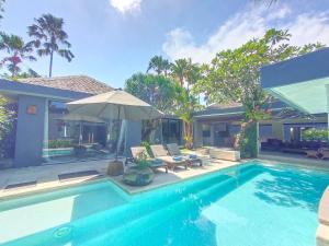 a swimming pool with an umbrella and a house at Kembali Villas in Seminyak