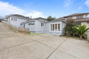 una casa blanca con una valla al lado de una entrada en Sun-Soaked Holiday Home Close to Beach, en Auckland