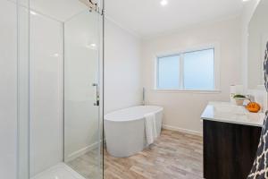 baño blanco con bañera y ducha acristalada en Sun-Soaked Holiday Home Close to Beach, en Auckland 4 fotos más