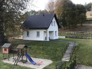 une petite maison blanche avec une aire de jeux dans la cour dans l'établissement Róża Sudetów Domek, à Duszniki-Zdrój