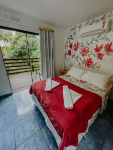 a bedroom with a bed with a red blanket and a window at Pousada Praia de Bombinhas in Bombinhas