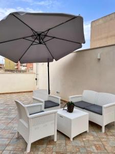 Un patio con sillas blancas y una sombrilla. en ALBARIA ROOMS-APARTMENTS, en Marsala
