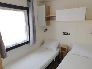 - 2 lits dans une petite chambre avec fenêtre dans l'établissement Mobilhome camping le MAR ESTANG, à Canet
