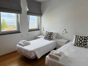 2 Betten in einem weißen Zimmer mit 2 Fenstern in der Unterkunft Casa dos Remedios in Angra do Heroísmo