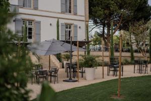 a patio with tables and chairs and an umbrella at Hôtel-Restaurant Villa Métis in Les Herbiers