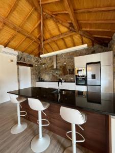 uma cozinha com um balcão preto e bancos brancos em Refúgio do Vale em Celorico de Basto