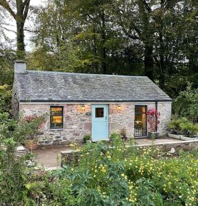 a stone cottage with a blue door in a garden at Charming stone Bothy at Loch Lomond in Luss