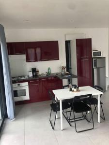 kuchnia z czerwonymi szafkami oraz białym stołem i krzesłami w obiekcie Charment logement avec parking et jardin privatif w mieście Rocbaron