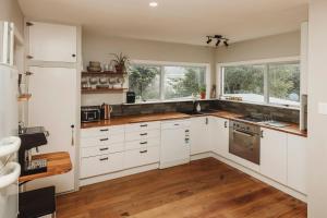 a kitchen with white cabinets and wood floors and windows at The Ocean Villa - Private Sauna in New Plymouth