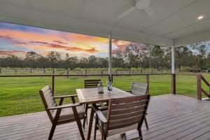 a table and chairs on a deck with a view of a field at 27 Rows on Hermitage in Pokolbin