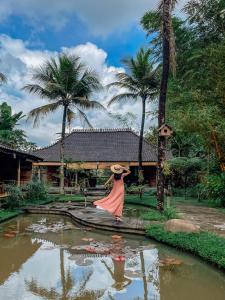 una mujer con un sombrero parada frente a un estanque en Korurua Dijiwa Ubud en Ubud