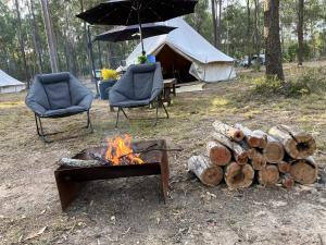une tente avec une cheminée, 2 chaises et un parasol dans l'établissement Childers Nature Camp, à Childers